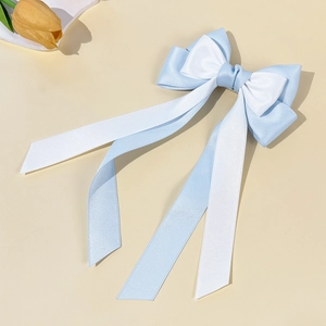 Detail of blue and white satin ribbon bow hair clip with long streamers on beige background