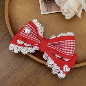 Detail van rode geruite haarclip met strik, witte kant en hartvormige parels