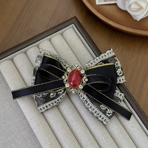 Vintage golden lace bow hair clip with red gemstone inlay on gray velvet background