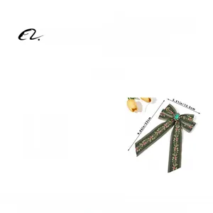 Detail of dark green embroidered bow hair clip with a green gemstone and pink floral pattern