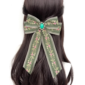 Detail of dark green bohemian bow hair clip with embroidery and green gemstone on long hair
