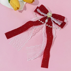 Close-up of red velvet bow hair clip with lace edges, pearl pendant, and gold accents