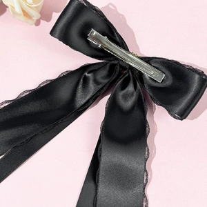 Elegant black satin lace bow hair clip with long ribbon tails on a soft pink background