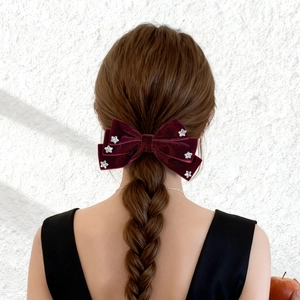 Close-up of a burgundy velvet bow hair clip with silver stars on a braided ponytail