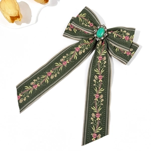 Close-up of Bohemian green fabric bow hair clip with floral embroidery and green gemstone
