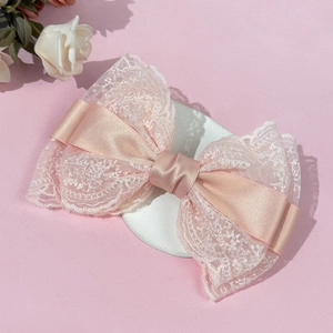 Close-up of pink lace and satin bow hair clip on a decorative white plaster display tray