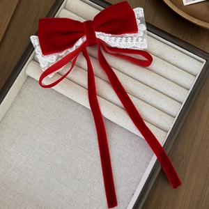 Close-up of red velvet bow hair clip with white lace trim and long flowing ribbons