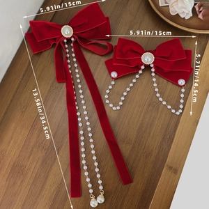 Red velvet bow hair clips with pearl tassels and crystal accents on wood surface