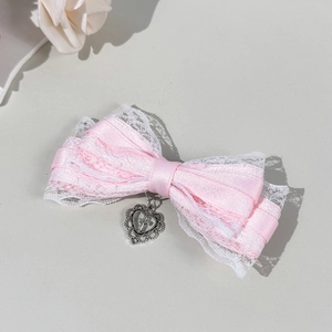 Détail de la pince à cheveux nœud rose avec dentelle et pendentif cœur argenté