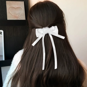 Vista dettagliata di un fermaglio per capelli in raso bianco con pompon e lunghi nastri