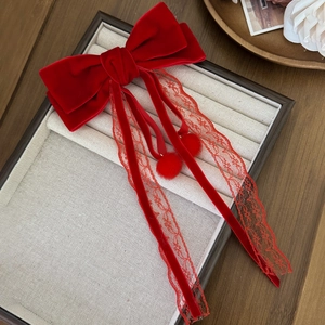 Detail of red velvet bow hair clip featuring delicate lace ribbons and fuzzy pom-poms