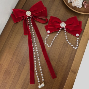 Elegant red velvet bow hair clip with faux pearl chain and streamers on dark wood background