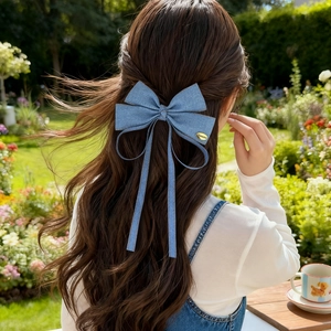 Detailed view of a blue denim bow hair clip with long ribbons on wavy brown hair
