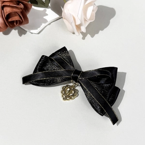 Detail of black satin bow hair clip with gold glitter edges and a heart cross pendant