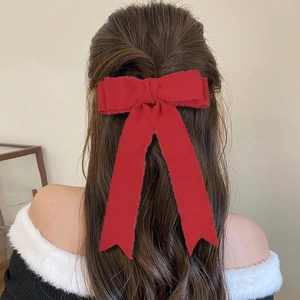 Close-up of a large red wool bow hair clip with long ribbons worn on a ponytail