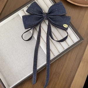 Denim bow hair clip with ribbons and gold metal tag on a jewelry display tray