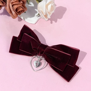 Détail de la barrette à nœud en velours avec pendentif cœur croix sur fond rose