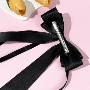 Elegant black satin bow hair clip with silver metal alligator grip on pink background