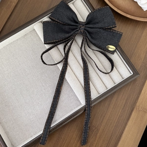 Detailed shot of dark denim bow hair clip with yellow stitching and gold Chanceux metal tag
