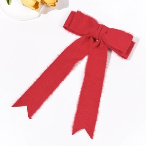 Detail view of a long red velvet bow hair clip with plush texture and elegant streamer