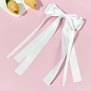 Detail view of a white satin bow hair clip with elegant long streamers on pink background