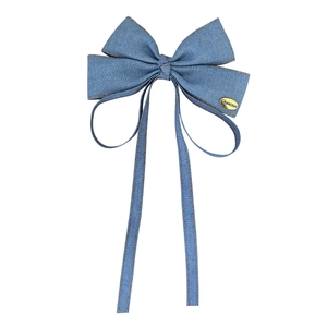 Denim bow hair clip with orange contrast stitching and long ribbons on white background