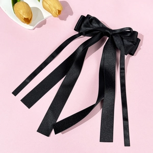 Close-up of black satin bow hair clip with long ribbons on an elegant pink background