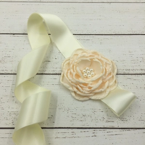 Detail of cream fabric flower belt with glossy satin ribbon and pearl center embellishment