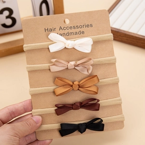 Detail view of five handmade polyester bow baby headbands on a kraft card packaging
