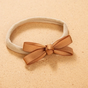 Detail of baby nylon headband featuring a double-layered caramel satin bow on beige band