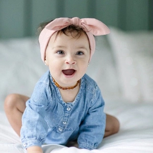Détail d'un bandeau en tricot rose avec nœud et un collier d'ambre pour bébé