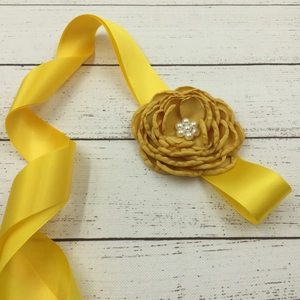 Detail of yellow satin floral belt featuring delicate fabric petals and pearl center decor
