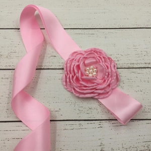 Close-up of pink satin belt with handmade fabric flower and white pearl center details