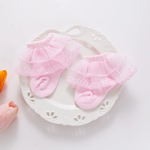 Detail of pink baby socks with delicate double-layered white lace trim on a white plate