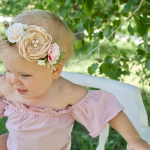 Détail d'un bandeau floral pour bébé avec rose champagne et perle sur un jeune enfant