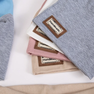 Detail of ribbed knit baby beanies with handmade faux leather labels in multiple colors