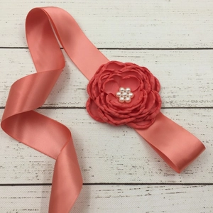 Detail of coral pink satin ribbon belt featuring a handmade fabric flower with pearl center