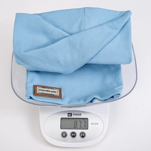 Light blue knitted baby beanie and scarf set weighing 87.7g on a digital scale