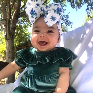 Detail of baby velvet green ruffle dress and large floral bow headband worn by a smiling baby