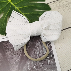 Detail of delicate white eyelet lace bow attached to a soft nylon baby headband