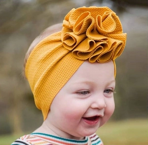 Gros plan d'un bandeau pour bébé jaune moutarde en tissu côtelé avec une grande fleur douce