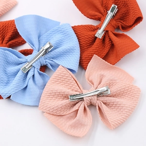 Detail of candy-colored fabric bow hair clips showing textured weave and metal alligator clips