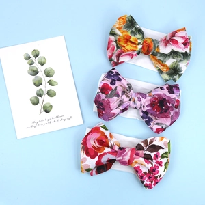 Detailed view of three baby headbands with floral bow prints on soft white fabric