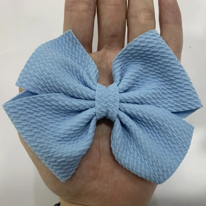 Detail of light blue waffle texture fabric bow hair clip held in hand for size