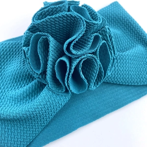Gros plan du bandeau bébé en maille gaufre bleu paon avec détail floral en tissu