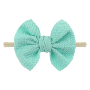 Detailed macro view of mint green ribbed bow on soft beige nylon baby headband