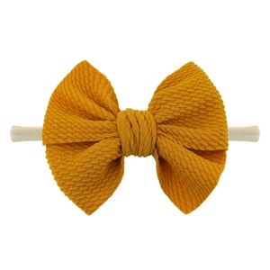 Detailed view of ginger yellow waffle texture bow on stretchy nylon baby headband