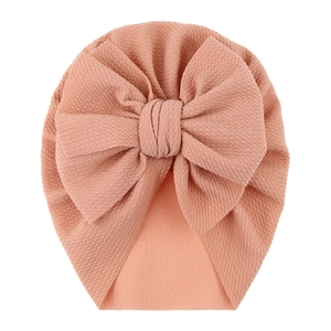 Close-up of peach pink infant turban hat featuring ribbed texture and a large bow detail