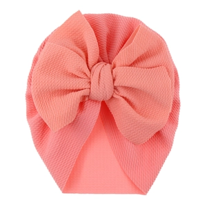 Detailed view of coral pink waffle knit baby turban hat with a large decorative bow