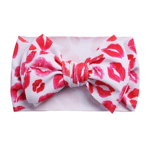 Close-up of white elastic baby headband with red lipstick kiss prints and a large bow